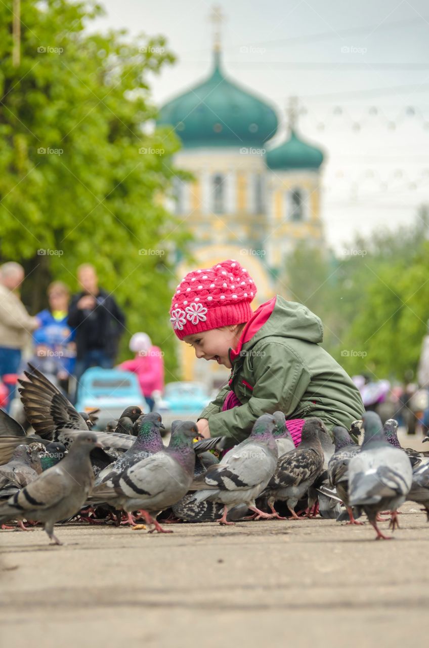 A little girl is playing in the city with pigeons.