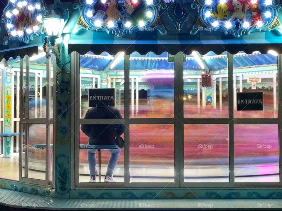 carousel spinning in a winter night with the carousel man sitting on a bench, streaks of lights