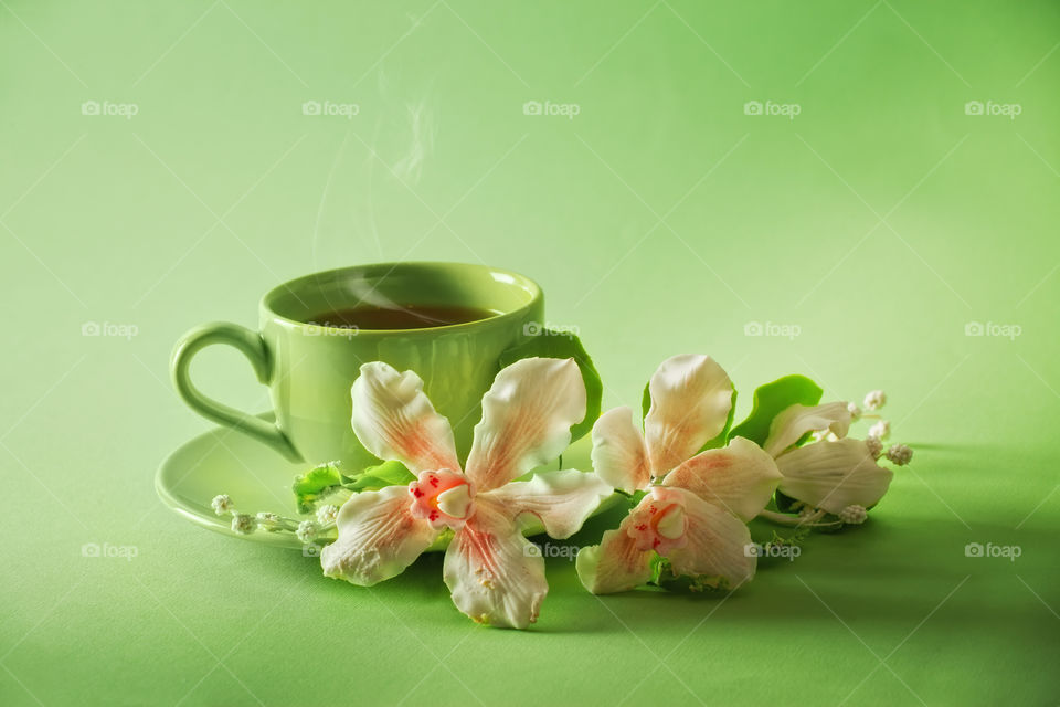 Green cup of green tea with caramel flowers on green background