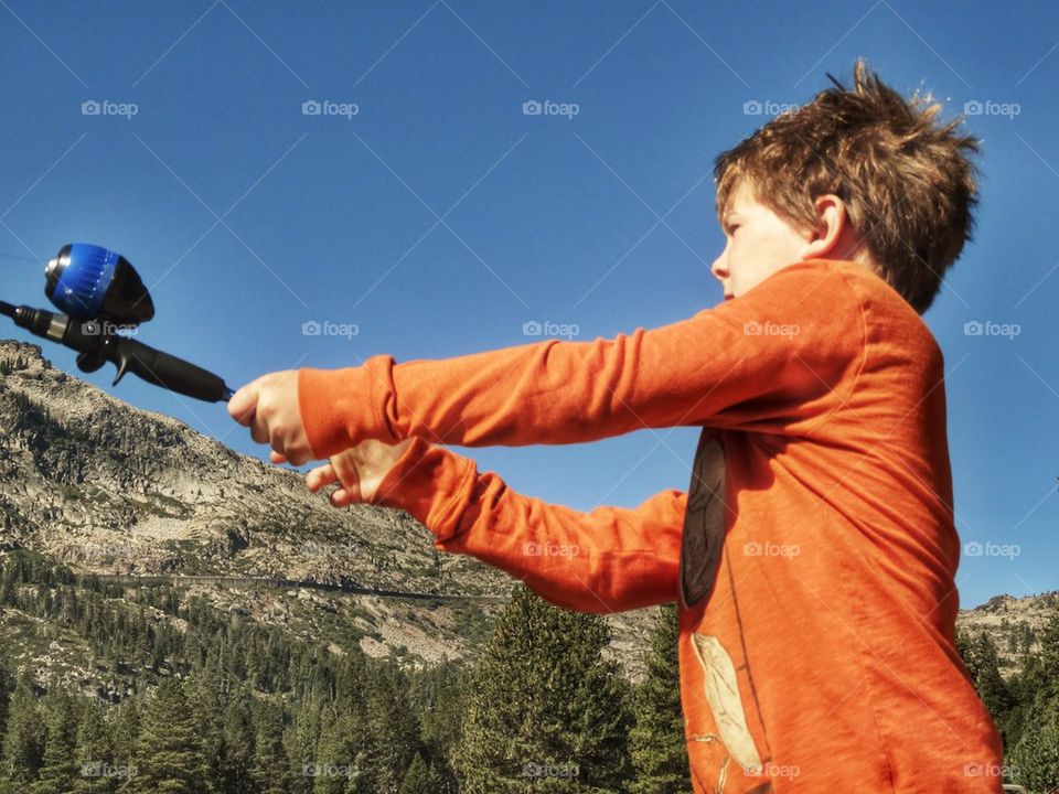 Young Fisherman Casting His Line At A Mountain Lake. Boy Fishing In The Summer
