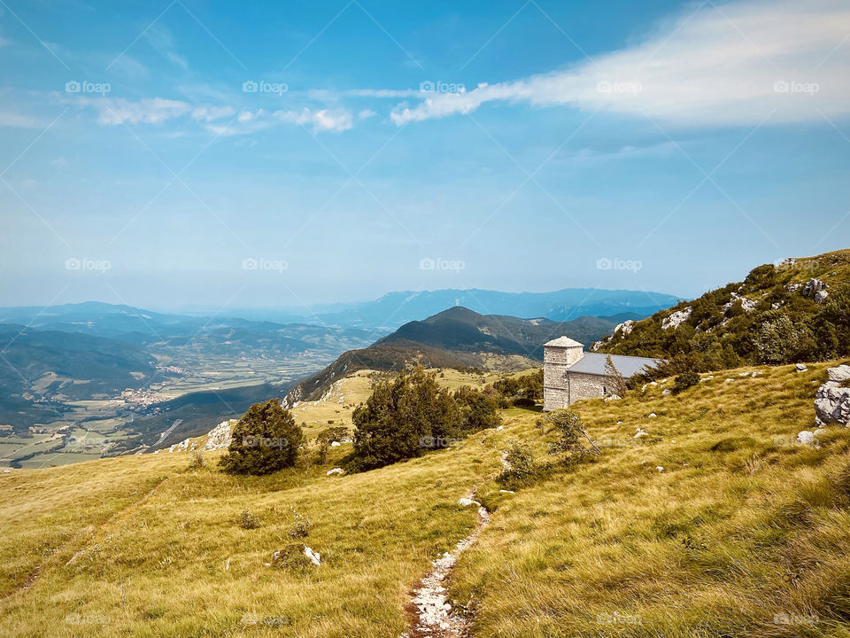 Scenic view of the old church in the small village at the green hills against blue sky in summer day. Nature landscape.