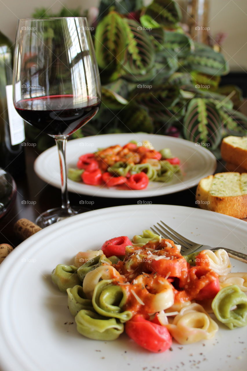 Italian inspired meal of tri-colored tortellini with red sauce and red wine.