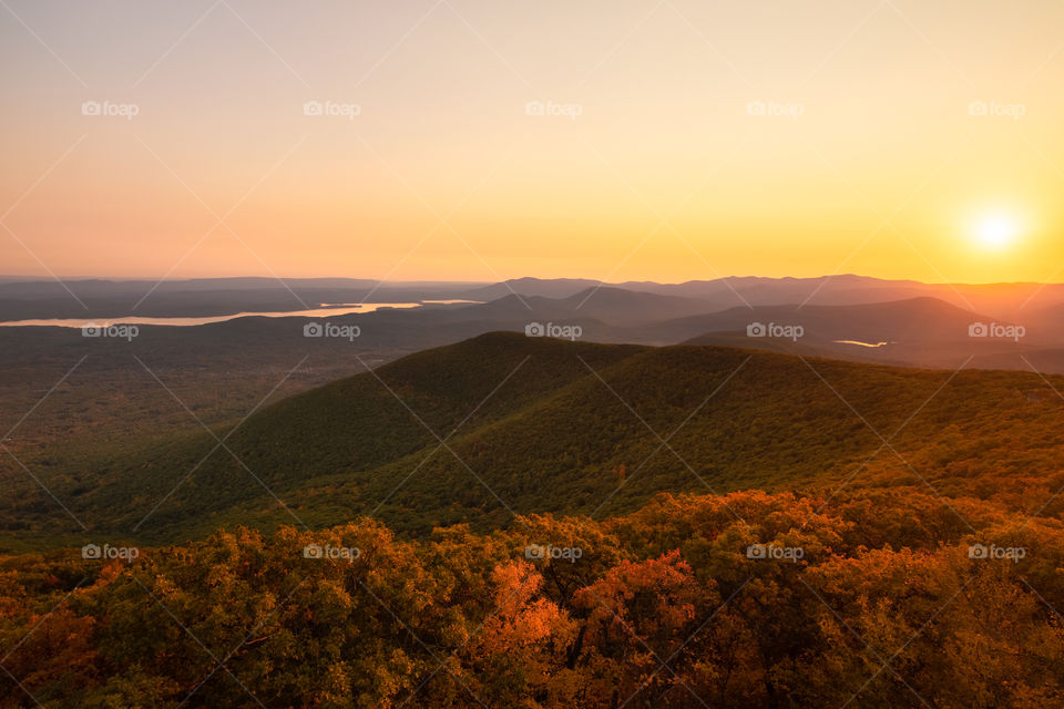 Warm golden light from a sunset washing over a mountain landscape covered in autumn fall foliage colors.