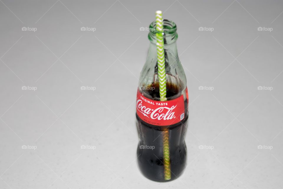 Bottle of Coca-Cola on a white background with a green and white straw.