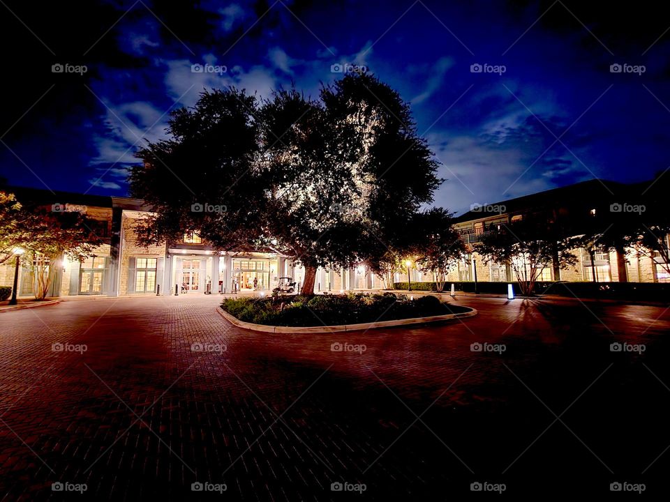 A distant lightning storm casts an eerie glow over a warmly lit courtyard