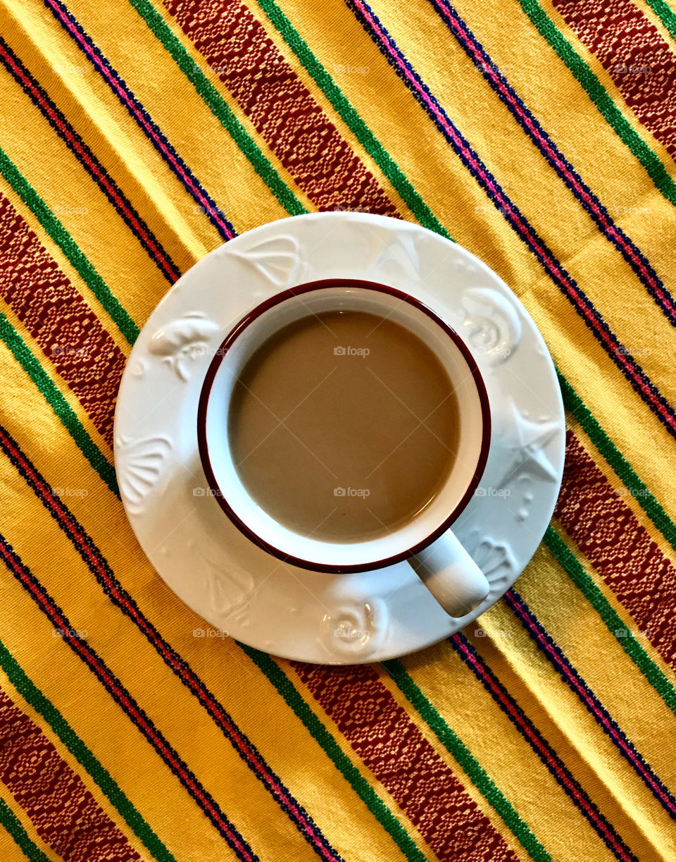 Hot cup of coffee against a bright yellow patterned table cloth