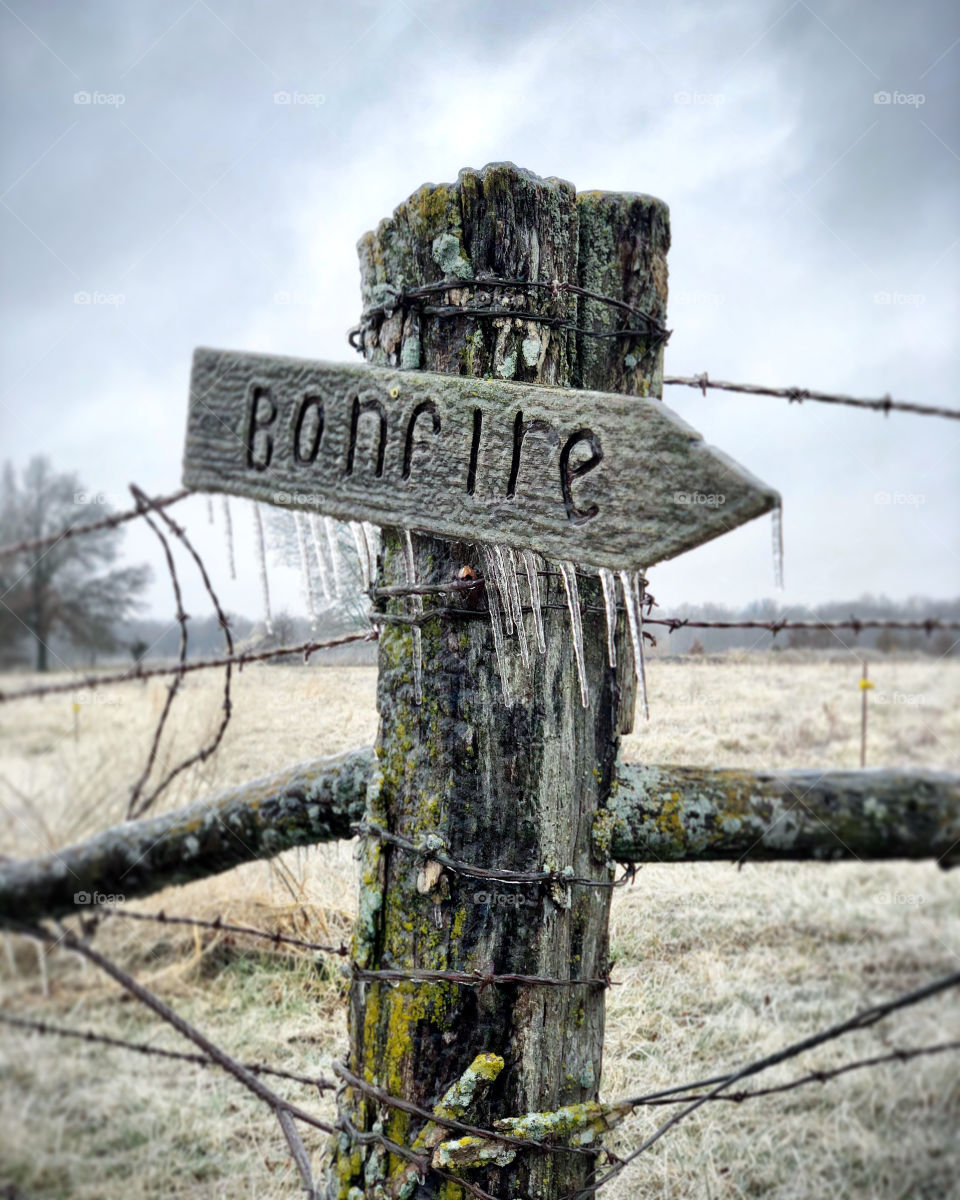 An old fence post directing to the bonfire frozen on a icy cold winter day.