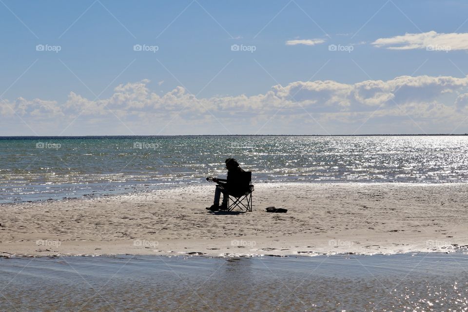 Lone guitarist singer sitting in chair surrounded by ocean 