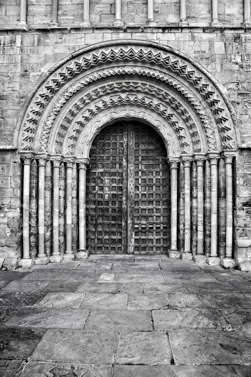 The entrance to an old church. A heavy wooden door to Selby Abbey in Yorkshire. Stone masonry carvings and pillars.
