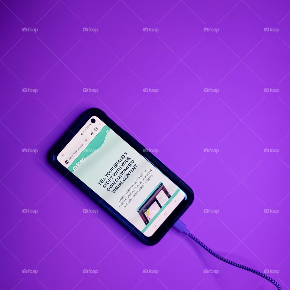 A simple flatlay of the foap phone app on a phone with a purple background and connected to a cord.