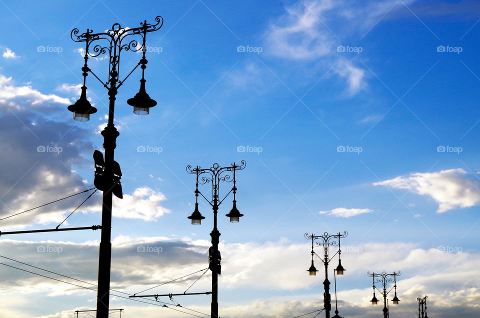 Low angle view of street light silhouettes against cloudy sky.