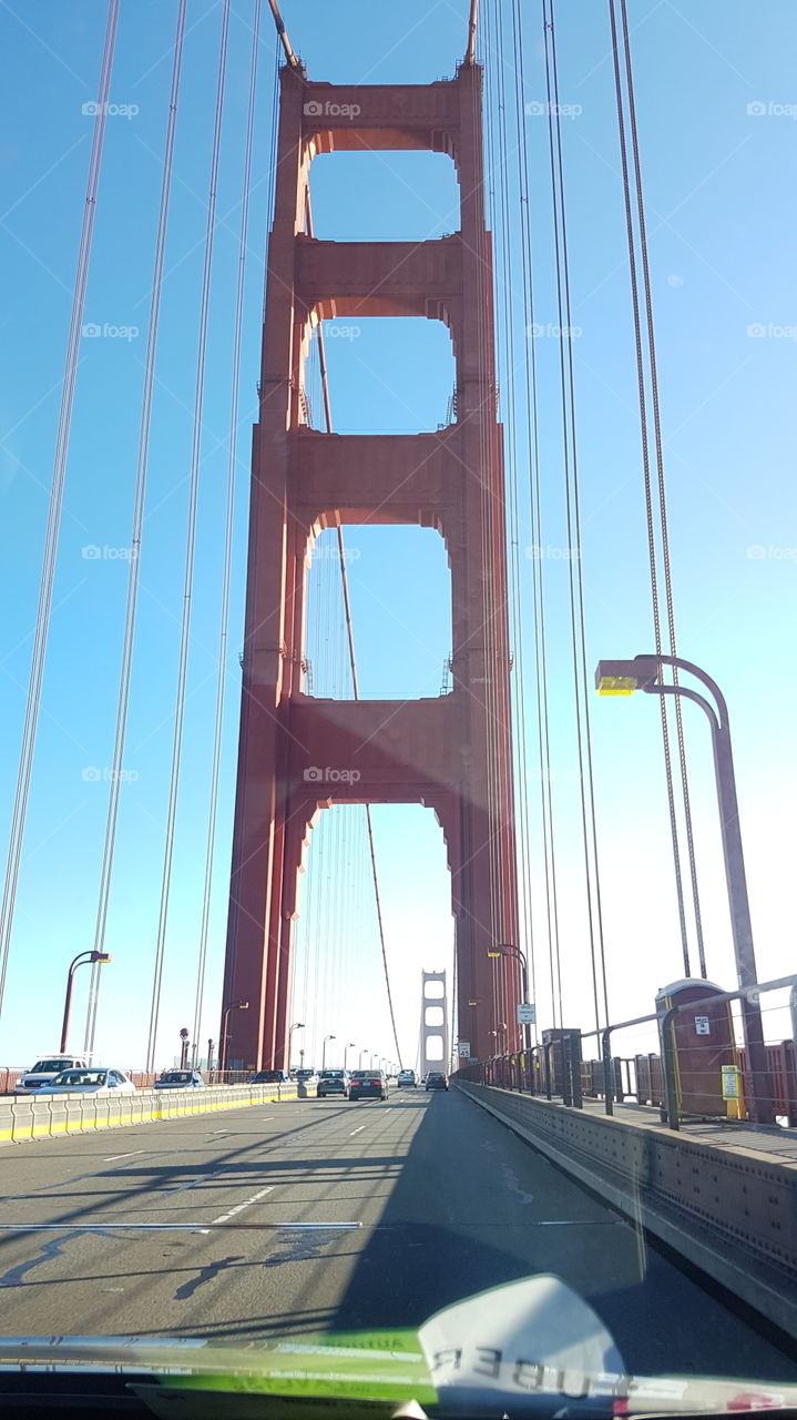 view from back window in Uber car ride, of the red colored Golden Gate Bridge in San Francisco, America, on happy sunny day with blue sky