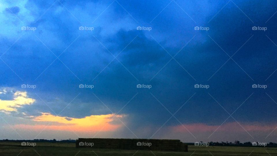 Sunset during storm over hay bails