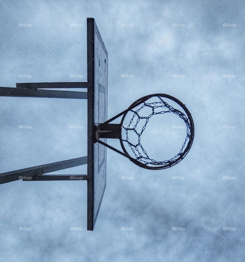 A beautiful photo of an old basketball net captured from underneath with the view of a cloudy winter sky in a school yard