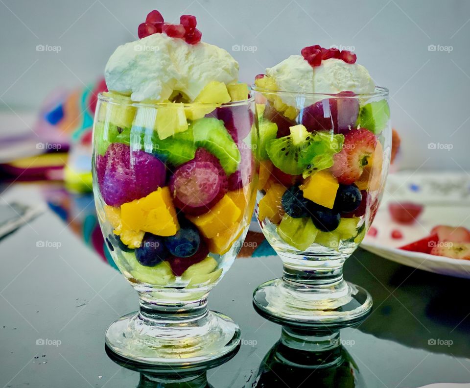Special fruit salad with ice cream for summer refreshment, contains mixed fruits slices like apple mango strawberry blueberry pineapple kiwi raspberry banana cherry and scoop of ice cream on top of it. Really a special food for summer season