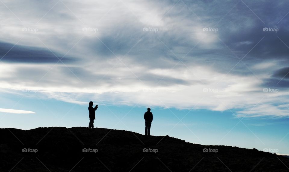 Silhouettes of two men on top of a mountain 