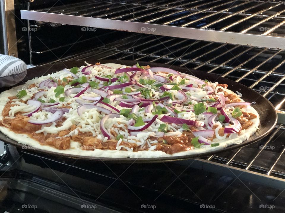 A BBQ chicken pizza getting ready to enter the oven. 