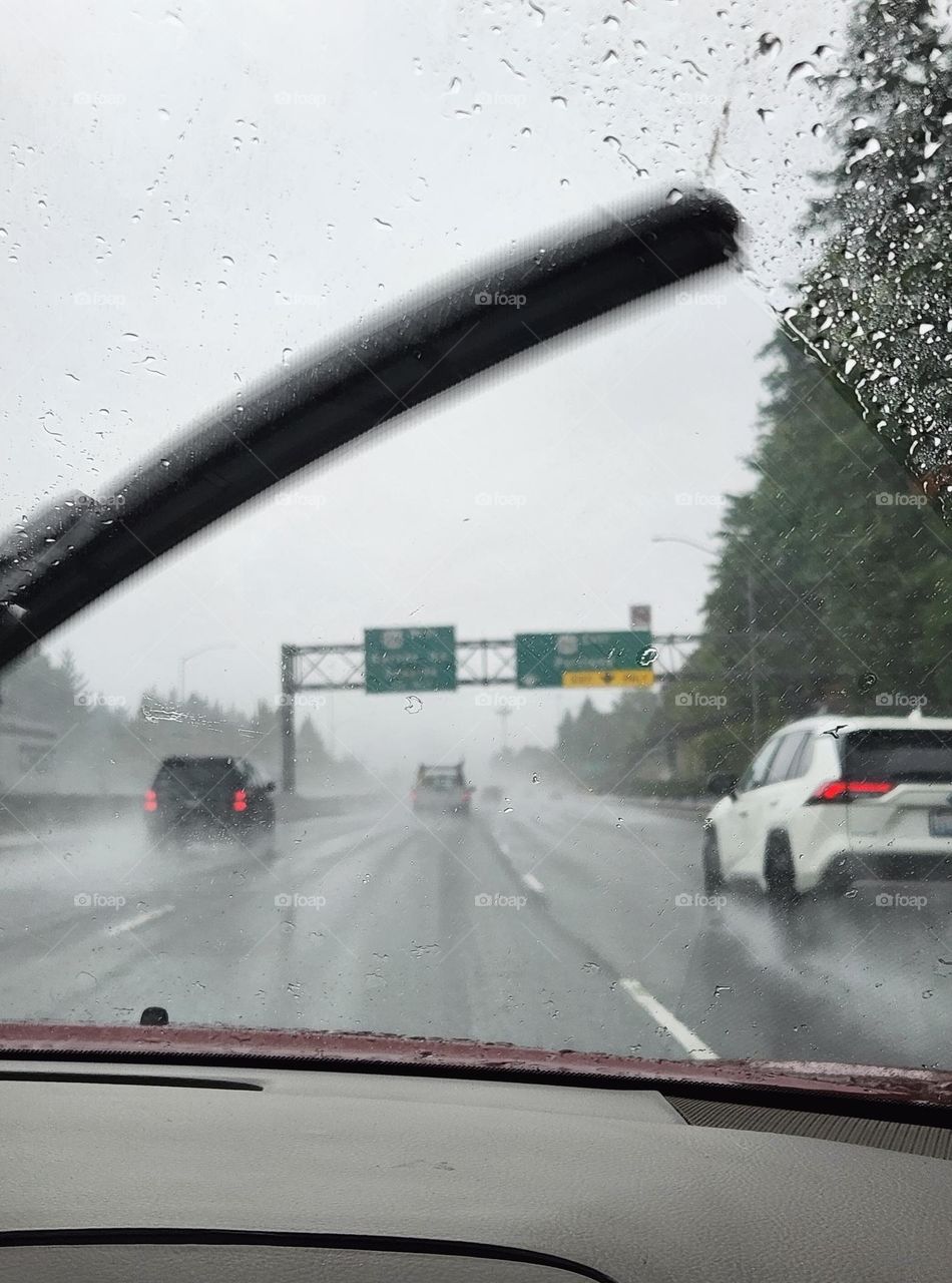 view of early morning commuter traffic in Oregon as seen through the windshield of a red car on a rainy day