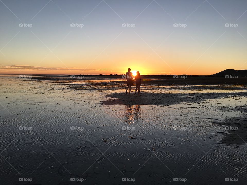 Silhouette couple walking in ocean water at low tide at sunset, romantic love dating relationship
