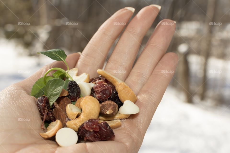 Healthy snacks - Holding a handful of fresh cashew nuts, almonds and antioxidant rich dried cranberry and blueberry mix outdoors with winter background and trees on a sunny day 