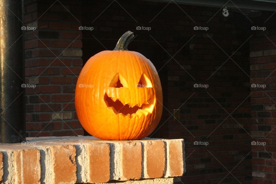 Carved pumpkin in sunlight on brick column in front of red brick house