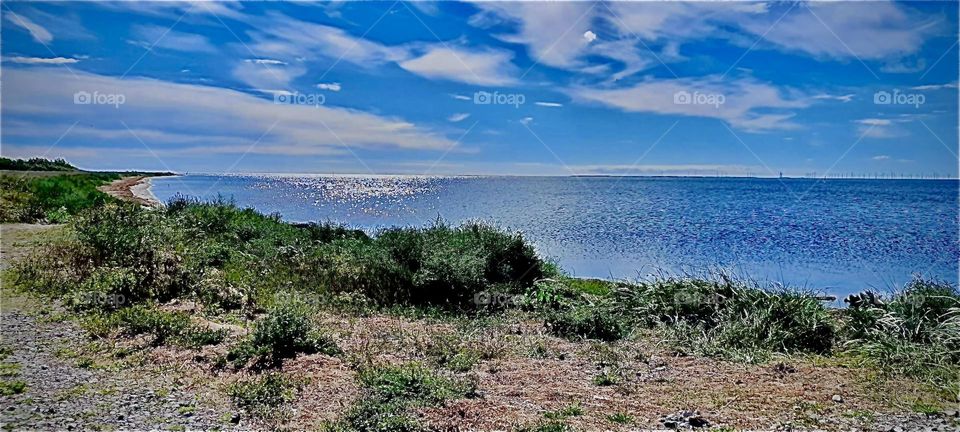 On a day trip to “Gedsen”, a small town in “Denmark” the “Ostsee”., the “East Sea” is glistening in beautiful shades of blue with sparkly silvery overlays. The sky has only a few large white clouds in it. 2022. Hypnotic Productions