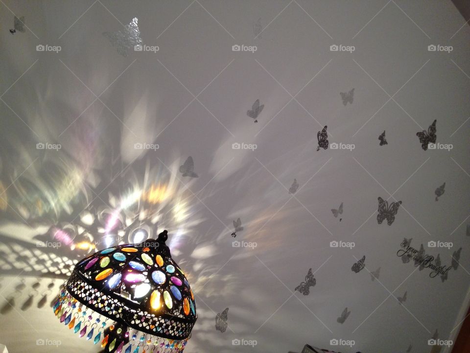 Light reflects thru stained glass lampshade onto wall with butterflies