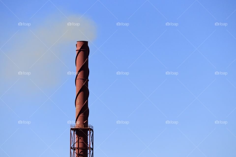 Large rusted metal mining industry tower blowing smoke into clear blue sky 