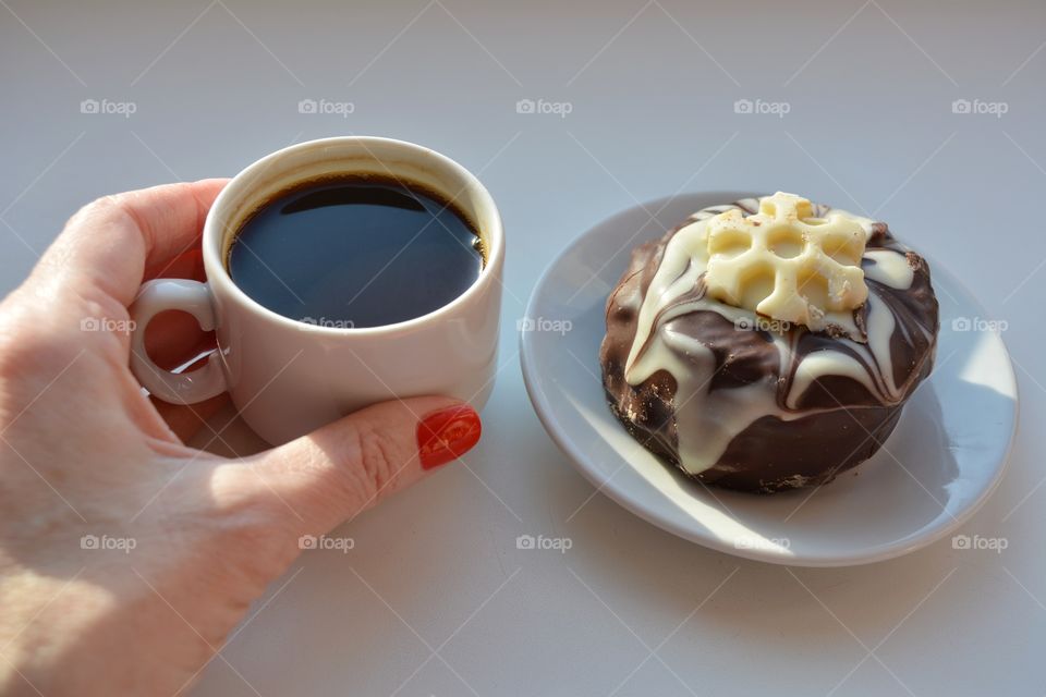 cup of coffee in the female hand and cake in sunlight on a white background