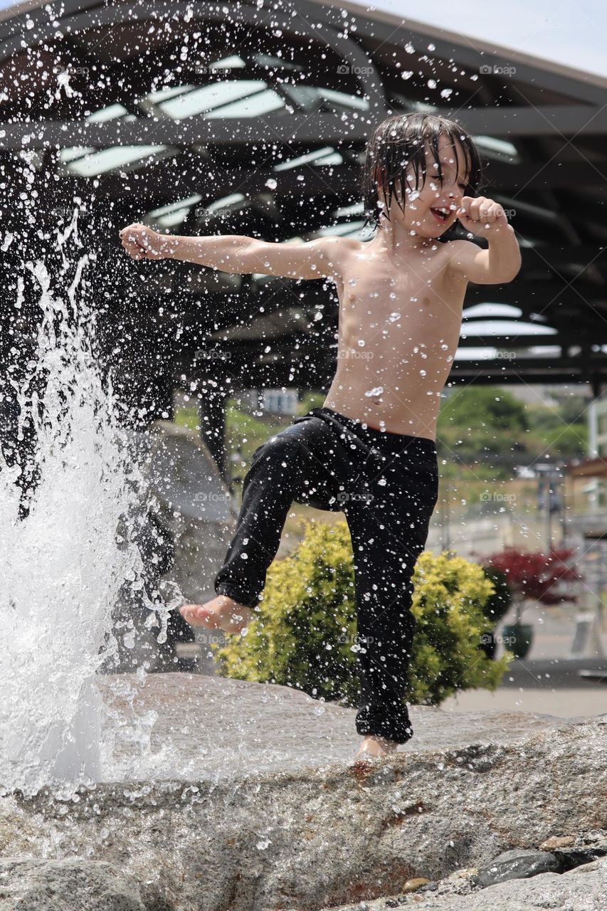 A vivacious young boy plays in the child friendly fountains at Point Ruston, Washington State 