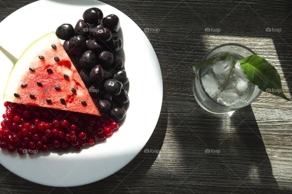 Cold, transparent drink with ice in a glass glass with summer snacks on a wooden background.