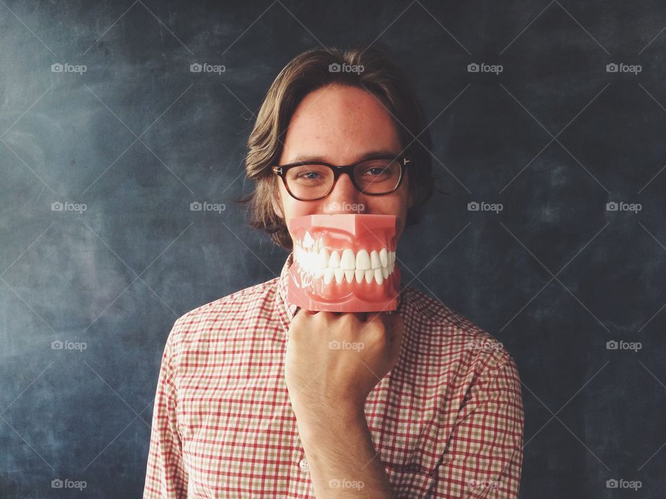 Big teeth. Man with big model of teeth in front of his mouth. 