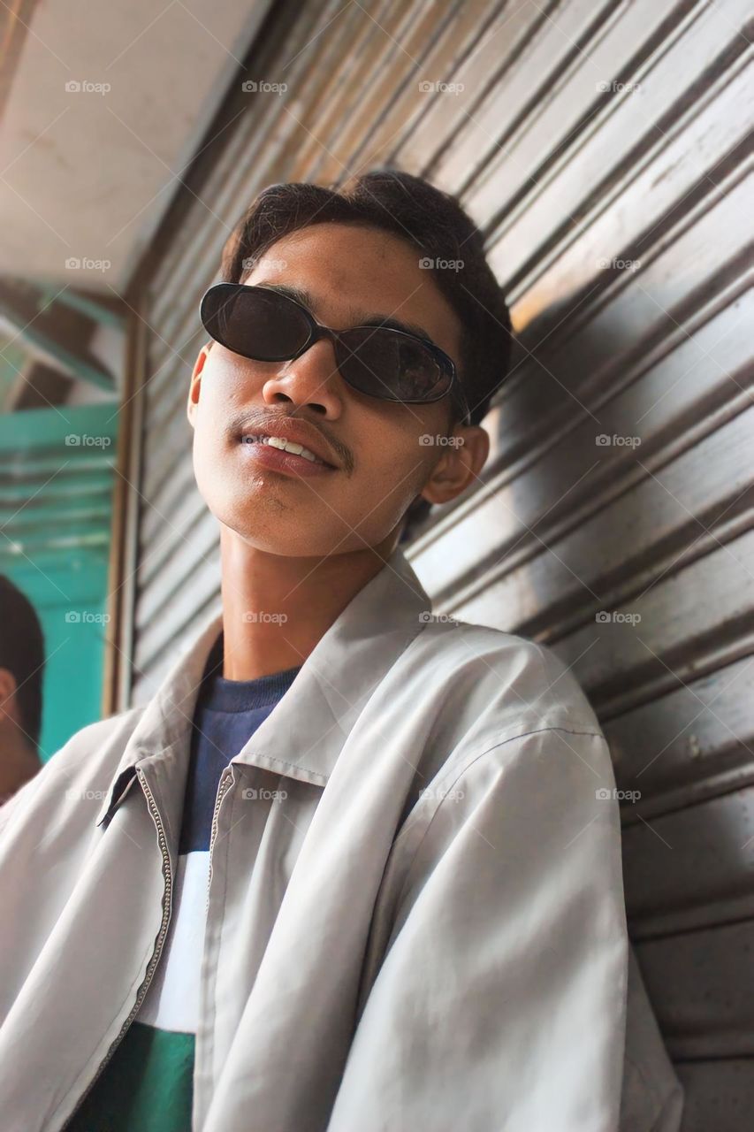 Portrait of young man wearing sunglasses while standing against wall