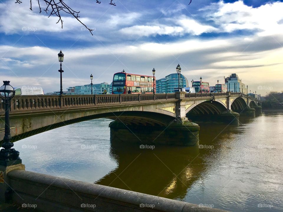 An iconic red double-decker zooms over a stately concrete bridge in London