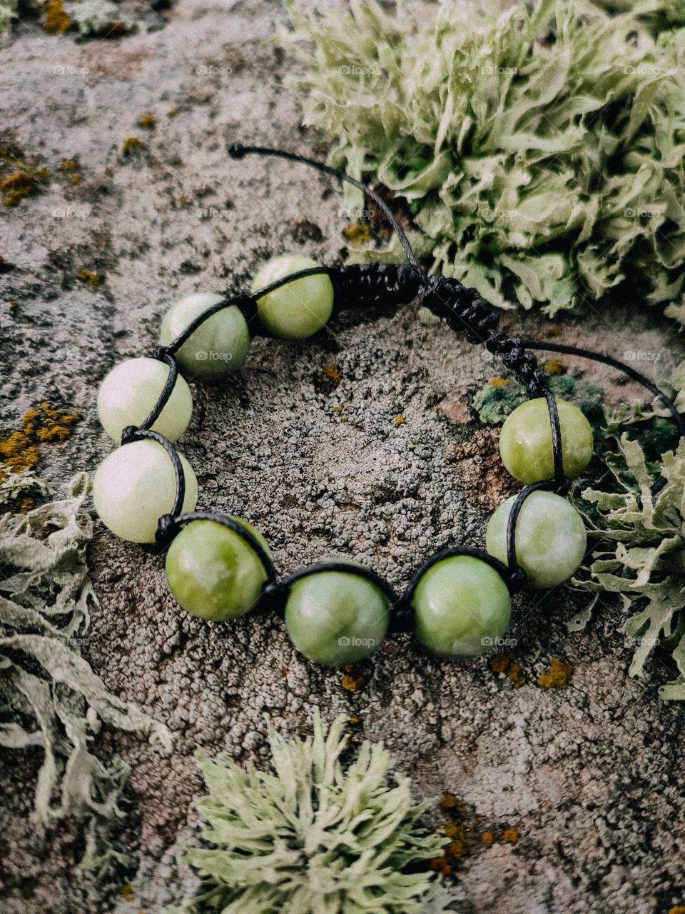 Green nephritis woven shamballa bracelet close up on stone lichen surface. Round beaded gemstone bracelet, jewelry, accessory