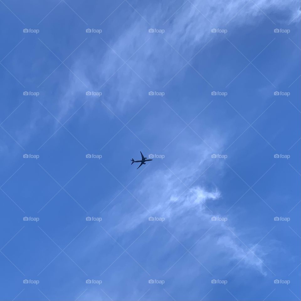 Solo, single airplane at the center of the blue sky flying. White clouds. Nature.