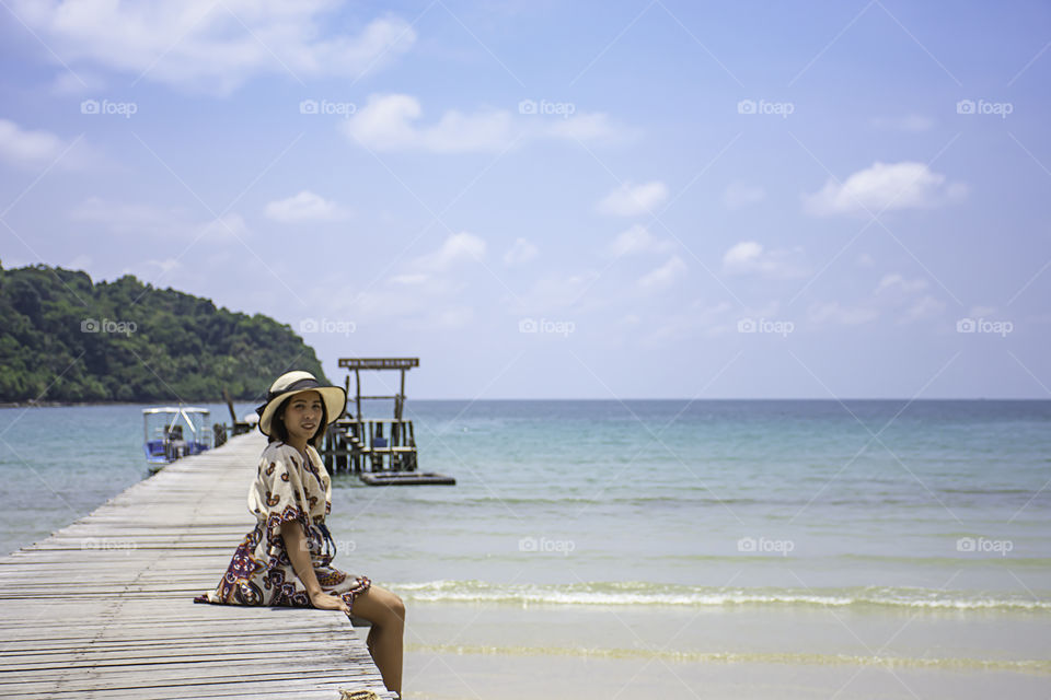 Women Wear a hat on the wooden bridge pier boat in the sea and the bright sky at Koh Kood, Trat in Thailand.