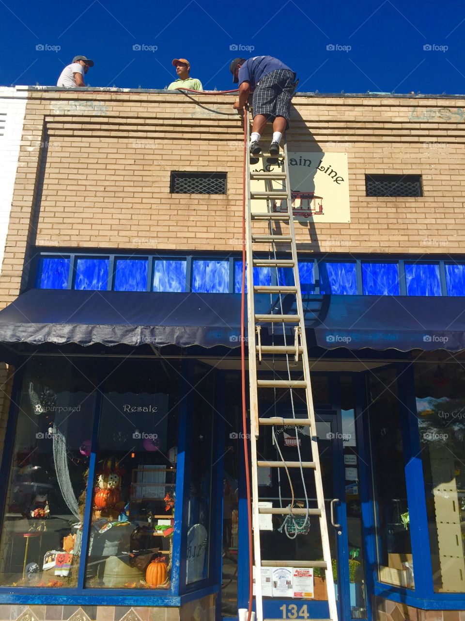 Workers painting a small business building standing on a roof and ladder with blue sky's above 