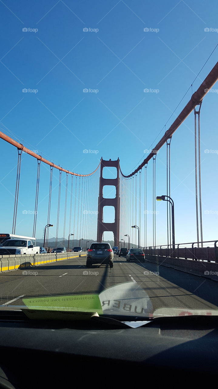 view from back window in Uber car ride, of the red colored Golden Gate Bridge in San Francisco, America, on happy sunny day with blue sky