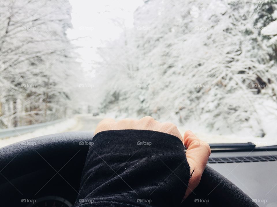 Hand on the steering wheel with snowy scenery seem through the windshield 