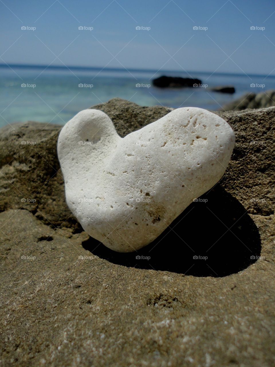 white stone heart on a sea stones shore summer time