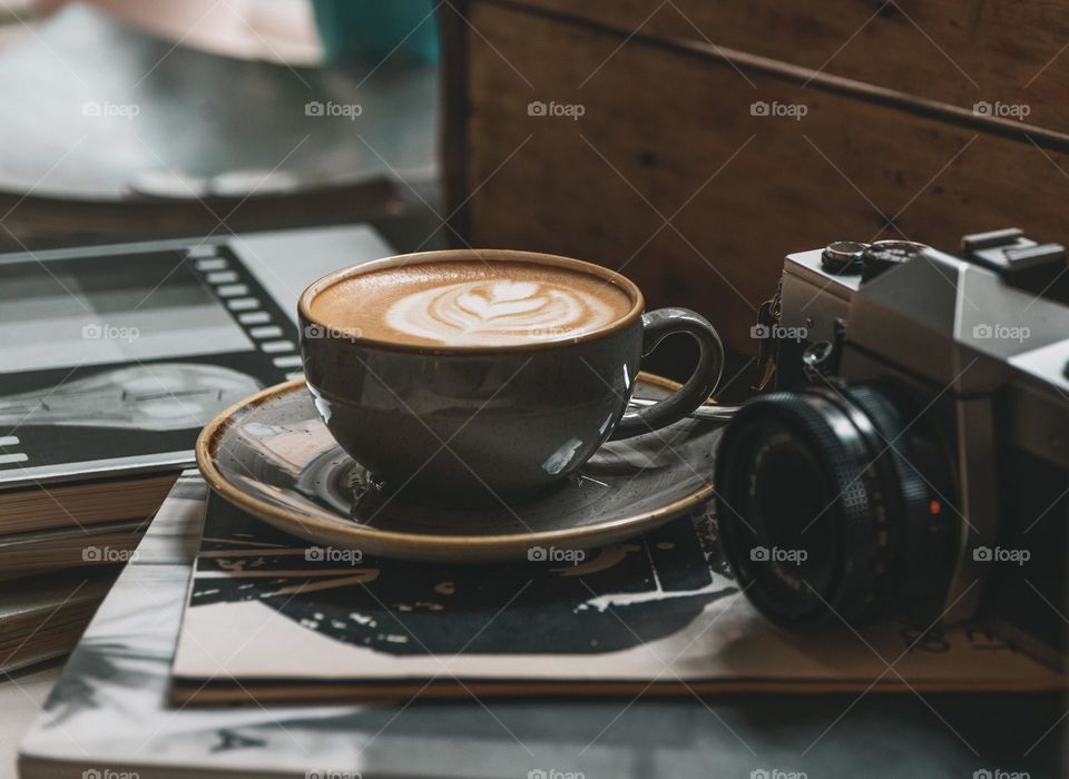 Close-up photo of cup of coffee with latte on table next to a vintage camera