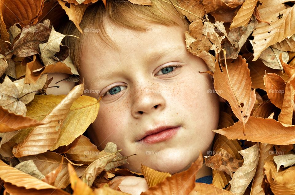 Close-up of boy covered in dry leaves