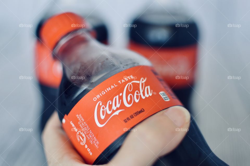 A persons hand holding a plastic bottle of coke 