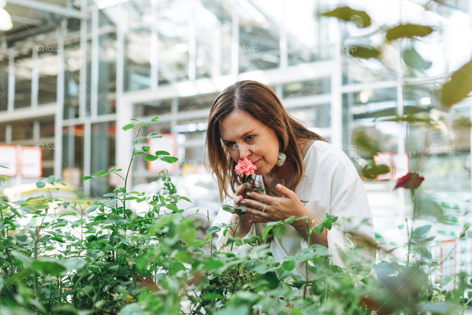 Brunette middle aged woman in white dress buys green potted house plants at the garden store