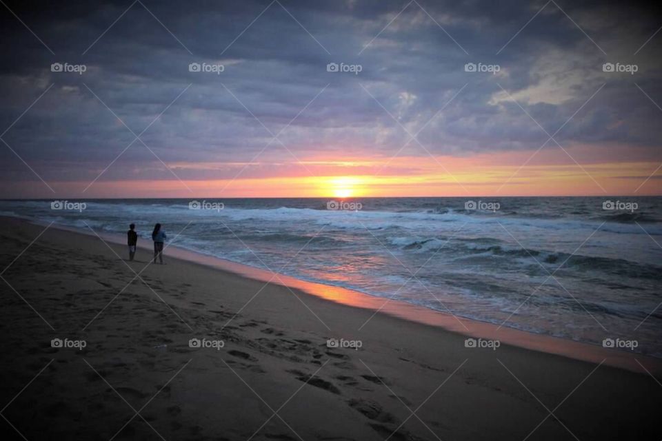 Young boy and girl standing along the sand watching the sun peak its way over the horizon. 
