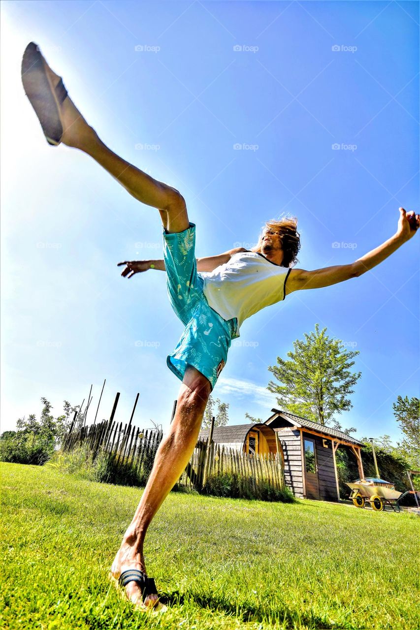 frog perspective portrait from a man kicking his leg high up in the air on a sunny day with blue skies