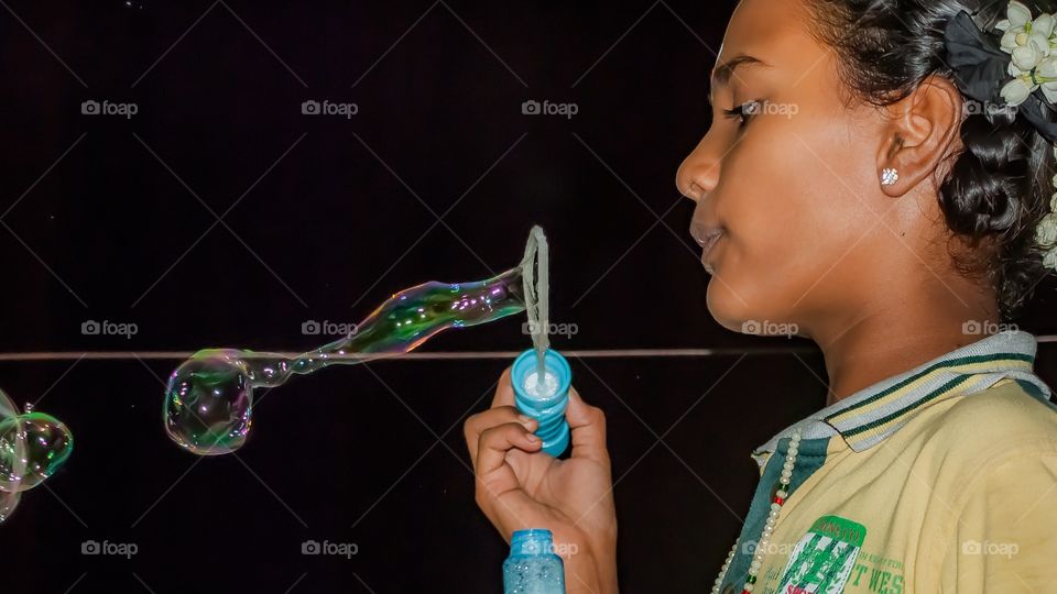 Teenager girl blowing bubbles against black background