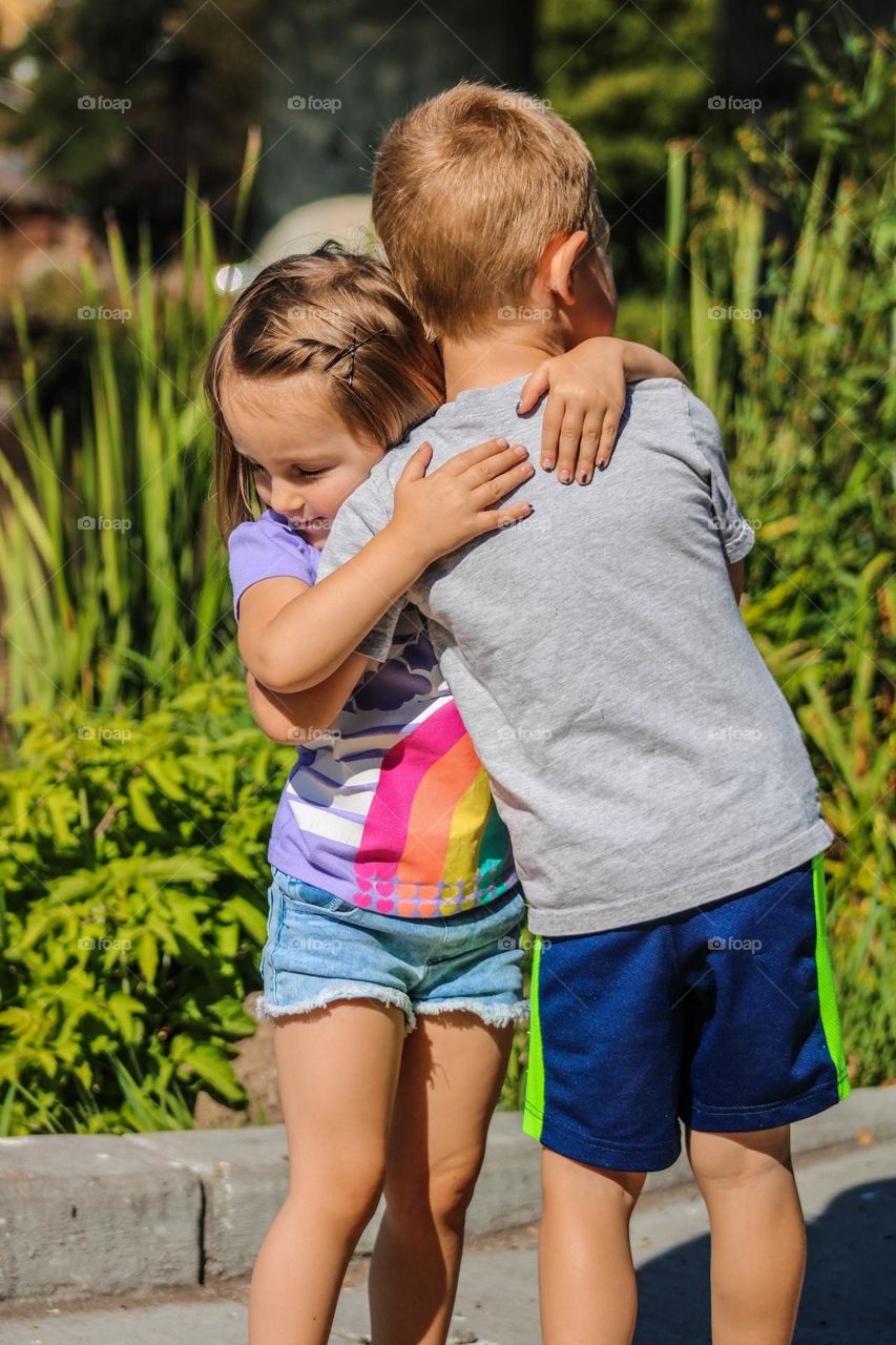 Close up of girl and boy toddler hugging in front of a grassy lake on a summer day in Oregon