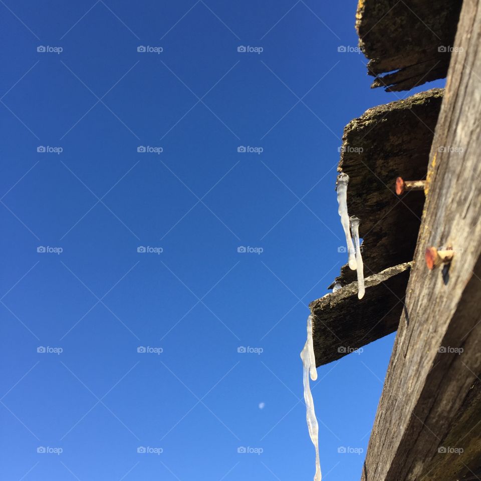 Icicles hanging from the rafters of a vintage farm building against a clear blue sky